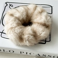 Dettaglio di un elastico per capelli in finta pelliccia beige su un libro d'arte sobrio - Albicocca Beige