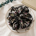Nahaufnahme eines floralen Satin-Haargummis auf einem Marmortablett mit Eukalyptusblättern - Schwarz Blumig