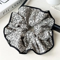 Makro-Detail von Blumen-Scrunchie mit schwarzer Paspelierung auf künstlerischem Hintergrund - Beige