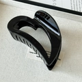 Detail of a gloss black heart-shaped hair claw clip on minimalist beige texture fabric - Black