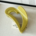 Detail of a glossy olive green heart-shaped hair claw clip on a decorative tray - Green