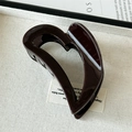 Detailed macro view of glossy burgundy heart hair claw clip on white textured tray - Brown