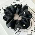 Detail of black satin scrunchie with white pearl trim on a white art book background - Black