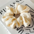 Close-up of beige satin scrunchie with white pearl embellishments on vintage book - Milky White