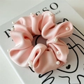 Detailed view of light pink satin scrunchie with white pearls on a minimalist book background - Pink