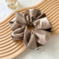 Close-up of champagne silk satin scrunchie featuring luxury pleated texture and woven label - Lazy Khaki