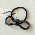 Detail view of dark tortoiseshell acetate bow hair tie on soft linen background - Amber