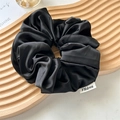 Macro shot of large black satin scrunchie with brand label on wooden tray decor - Elegant Black