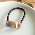 Detailansicht eines Acetat-Haargummis mit Bernsteinmuster und goldenem handgefertigtem Text - Blau Braun Beige
