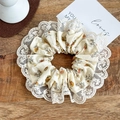 Detailansicht eines Vintage-Blumen-Scrunchies mit weißer Spitzenstickerei auf Holzgrund - Spitzenbesatz Blumen Khaki