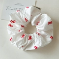 Gros plan sur un chouchou blanc avec motifs de nœuds rouges et étiquette tissée soignée - Blanc avec noeud rouge