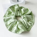 Detailed view of light green satin scrunchie with layered pleats and reinforced stitching - Green