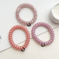Détail de trois élastiques spirale en rose et lavande avec petites étiquettes noires - Série Pâte de Haricot