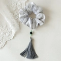 Détail d'un chouchou à fleurs à l'encre avec pompon et perles vertes sur fond de dentelle blanche - Gris