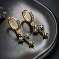 Détails macro de boucles d'oreilles croix dorées avec zircons bleus sur fond noir - Or Zircone Bleue