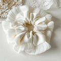 Détail d'un chouchou en satin blanc crème avec bords plissés et texture délicate - Blanc laiteux