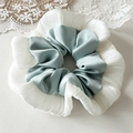 Gros plan d'un chouchou en satin bleu et volants blancs sur un fond en dentelle - Bleu