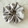 Detail view of large silver grey satin scrunchie on elegant white lace background - Gray