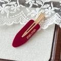 Makro-Detail der burgunderroten Acetat-Haarklammer mit Gold-Logo auf weißer Spitze - Rot