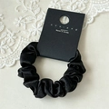 Detailopname van zwarte satijnen scrunchie met zijdezachte textuur en plooien - Zwart