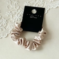 Close-up van champagne satijnen scrunchie met zachte geplooide textuur en kant decoratie - Melkwit