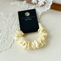 Dettaglio di uno scrunchie in raso giallo crema con pieghe su sfondo di pizzo bianco - Giallo