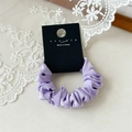 Dettaglio dell'elastico per capelli in raso lavanda su cartoncino nero e pizzo bianco - Viola