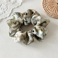 Detail eines Blumen-Seiden-Haargummis mit Bändern und Mustern auf Spitzenhintergrund - Haargummi-Stil / Grün