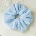 Detailed macro view of light blue pleated fabric scrunchie with handmade woven label - Blue