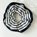 Detailweergave van de gestreepte stoffen scrunchie met zwarte ruches op een beige ondergrond - Zwarte Rand Gestreepte Klein