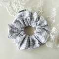Détail d'un chouchou à carreaux gris avec strass et étiquette en tissu sur fond neutre - Gris