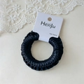 Detail view of a black satin scrunchie with pleated texture on a product display card - Black