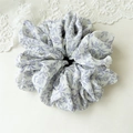 Dettaglio dell'elegante scrunchie floreale con stampa viola su morbido tessuto a pieghe - Foglia Di Bambù Viola