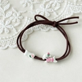Close-up of brown elastic hair tie with cute cartoon dog and bone pendants on lace background - Pink Puppy + Bone
