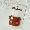 Close-up of a brown leather teddy bear hair clip with embroidery on a lace background - Shy Bear