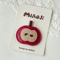 Detailed close-up of a red leather apple hair clip with fine stitching on a lace display - Apple