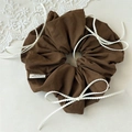 Detail van donkerbruine scrunchie met kanten strikjes en merklabel op crème basis - Koffie Strik Scrunchie