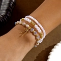 Detalle de pulseras de perlas en capas con cerámica azul y un lazo dorado elegante - Rosa Púrpura
