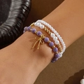Conjunto de tres pulseras de perlas y cerámica con dije de lazo dorado en la muñeca - Púrpura