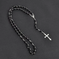 Elegante collar de rosario negro con colgante de cruz plateada sobre fondo gris oscuro - Negro