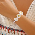 Detalle de una pulsera tejida bohemia con flores de plumeria y centros de pedrería - Blanco