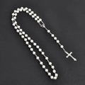 Detalle de collar de perlas con colgante de cruz plateada texturizada en fondo gris - Blanco