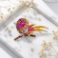 Détail macro de broche oiseau émaillé avec pierre rose et strass sur plateau en marbre - Rouge