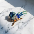 Détail macro de la broche oiseau montrant les plumes en émail et les strass brillants - Bleu