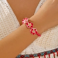 Detalle de pulsera tejida rosa ajustable con flores de plumeria rojas y cristales - Rojo