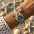 Adjustable gold starfish bangle with pearls and blue enamel worn on a beach setting - Blue Pearl Starfish (BR26Y0029-3)