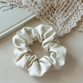 Detailed view of cream PU leather scrunchie showing premium texture on vintage art books - White