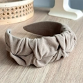Vista detallada de la diadema de tela plisada beige con nudo elegante sobre base de madera - Caqui