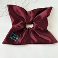 Close-up of wine red oversized silk scrunchie with handmade tag on white lace backdrop - Burgundy