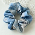 Detailansicht eines blau marmorierten Satin-Scrunchies mit weißem Spitzenhintergrund - Ölgemälde Blau Haargummi